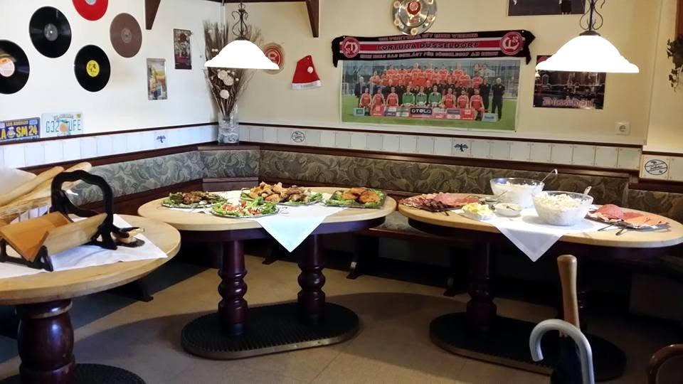 Die Gaststube mit runden Holztischen und Polsterbänken, an der Wand ein Mannschaftsfoto von Fortuna Düsseldorf.