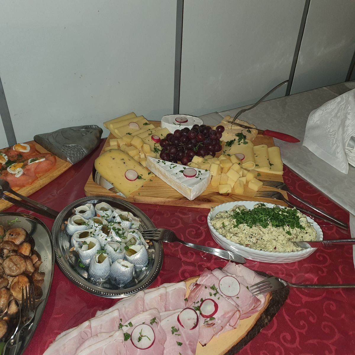 Käseplatte mit Trauben, daneben Rollmöpse, Schinken und Lachs mit Ei.