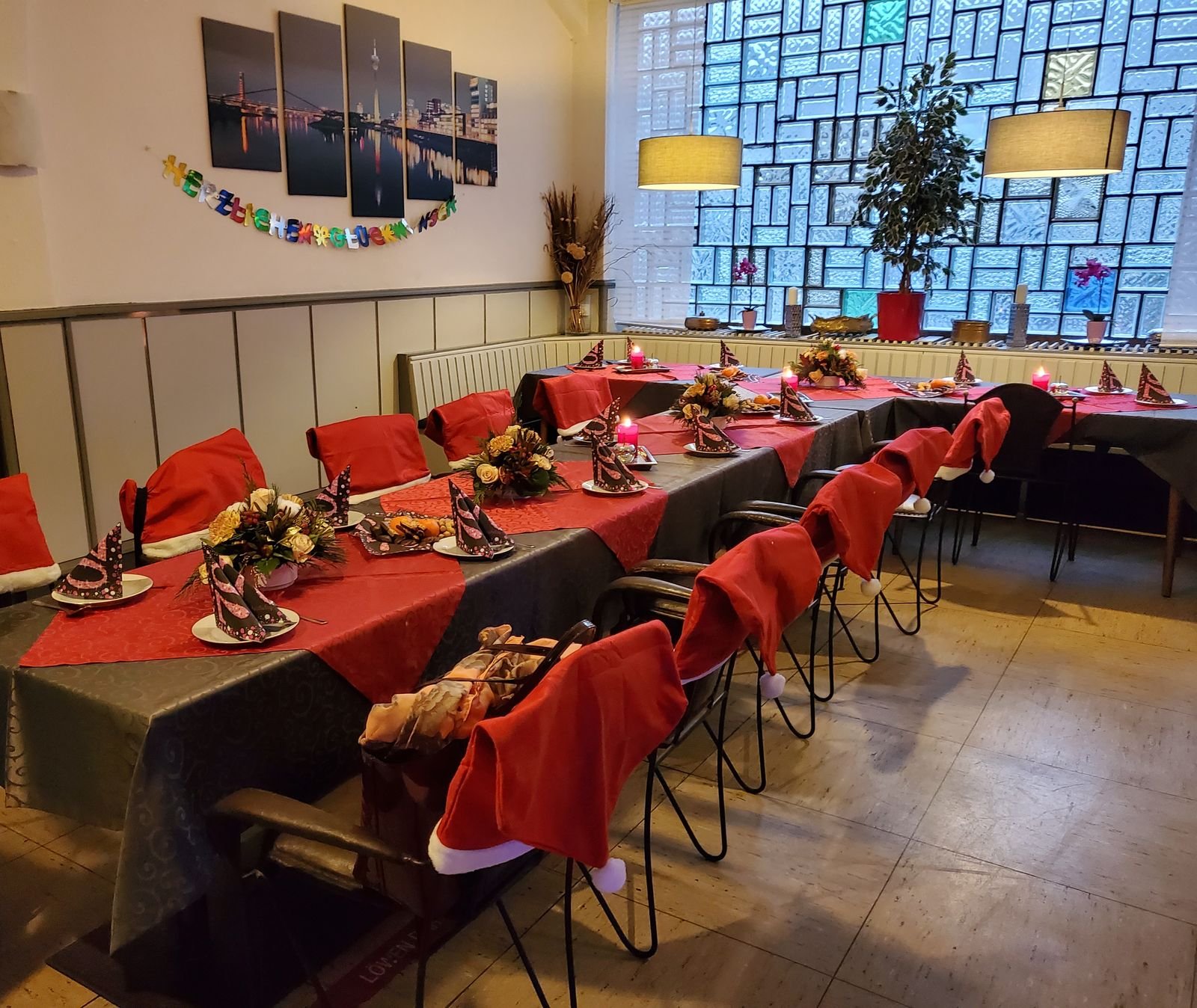 Der Saal, festlich gedeckt mit roten Tischläufern, Blumengestecken und Kerzen, die Stühle mit roten Hussen.